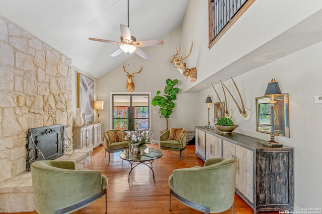 living room featuring ceiling fan, a stone fireplace, and hardwood / wood-style floors