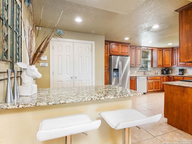 kitchen with a breakfast bar area, light tile patterned floors, kitchen peninsula, stainless steel appliances, and decorative backsplash