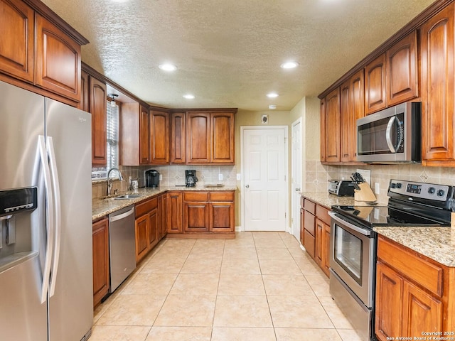 kitchen featuring light tile patterned flooring, sink, light stone counters, stainless steel appliances, and backsplash