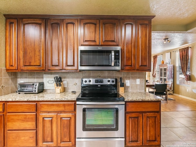 kitchen with stainless steel appliances, light tile patterned floors, light stone counters, and decorative backsplash