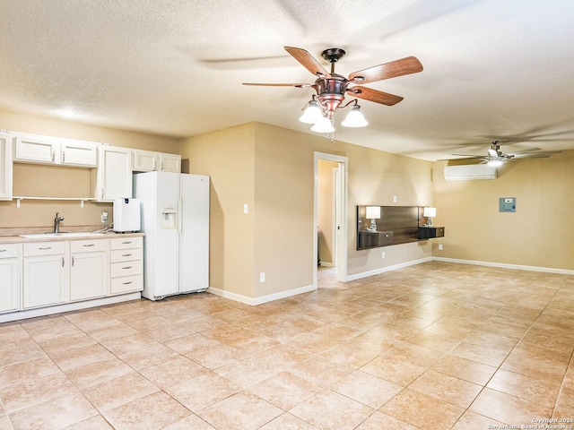 kitchen with sink, a wall mounted AC, white fridge with ice dispenser, a textured ceiling, and white cabinets