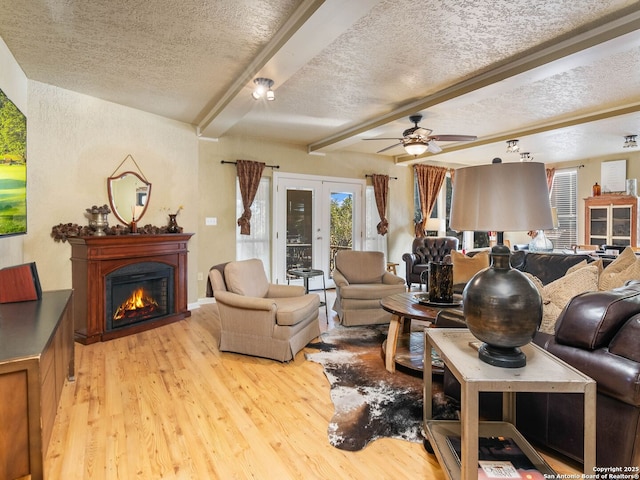 living room with french doors, a textured ceiling, light wood-type flooring, beamed ceiling, and ceiling fan