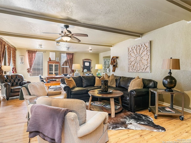 living room with beamed ceiling, ceiling fan, light hardwood / wood-style floors, and a textured ceiling