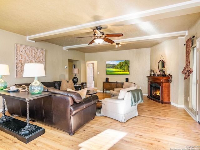 living room featuring beamed ceiling, ceiling fan, a textured ceiling, and light hardwood / wood-style floors