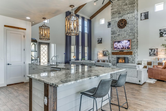 kitchen with a stone fireplace, a sink, light wood-type flooring, light stone countertops, and an inviting chandelier