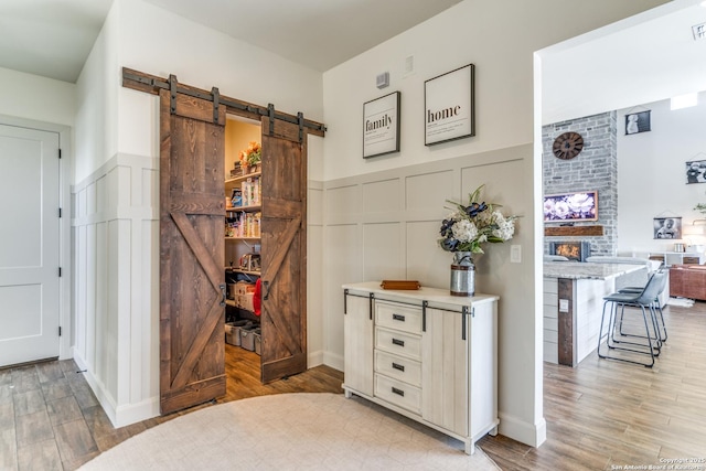 interior space featuring a barn door, a decorative wall, visible vents, light wood-style floors, and wainscoting