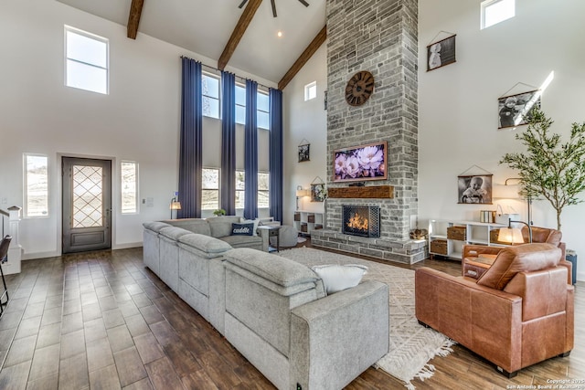 living area featuring dark wood-style floors, a wealth of natural light, beamed ceiling, and a stone fireplace