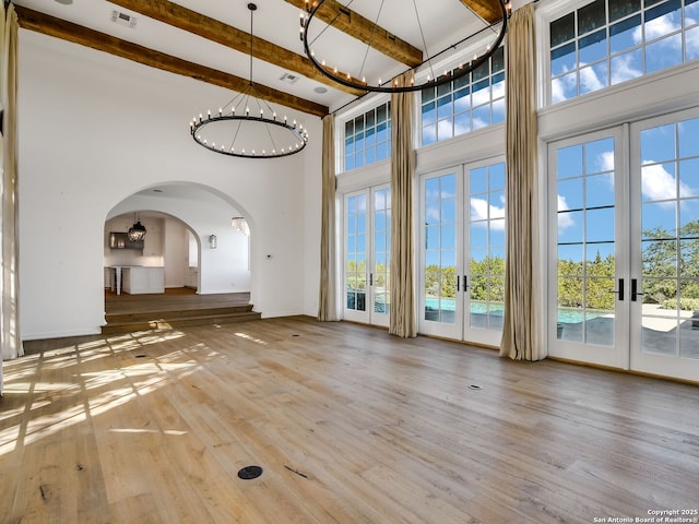 unfurnished living room with beam ceiling, wood-type flooring, french doors, and a high ceiling