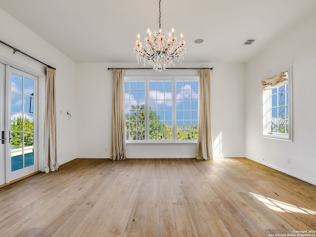 unfurnished dining area with a healthy amount of sunlight, an inviting chandelier, light wood-type flooring, and french doors