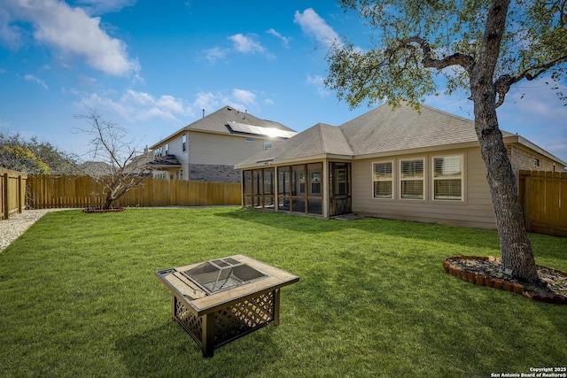 back of property with roof with shingles, a lawn, a sunroom, a fenced backyard, and a fire pit