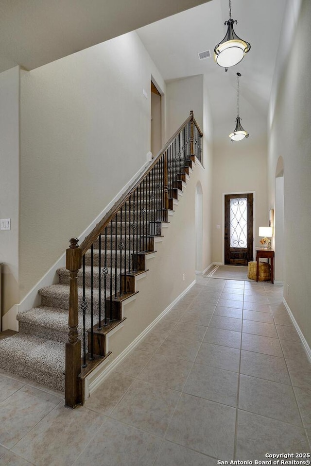 tiled foyer entrance featuring arched walkways, a high ceiling, stairs, and baseboards