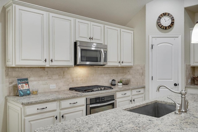 kitchen with light stone counters, stainless steel appliances, backsplash, white cabinetry, and a sink