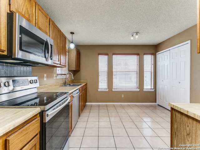 kitchen featuring sink, a textured ceiling, light tile patterned floors, appliances with stainless steel finishes, and pendant lighting