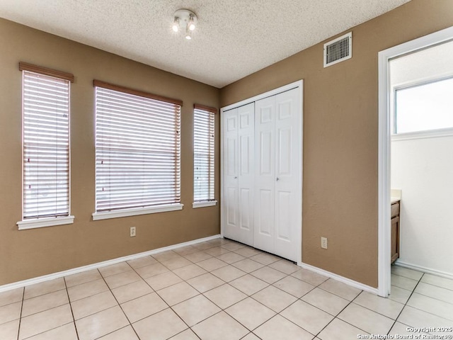 unfurnished bedroom with a closet, a textured ceiling, multiple windows, and light tile patterned floors