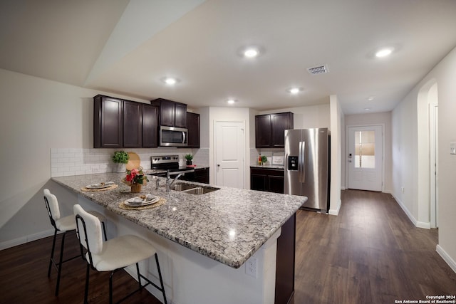 kitchen featuring dark brown cabinetry, stainless steel appliances, kitchen peninsula, and a kitchen bar