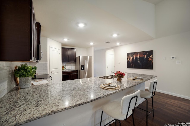 kitchen with light stone counters, stainless steel fridge with ice dispenser, dark brown cabinetry, and kitchen peninsula