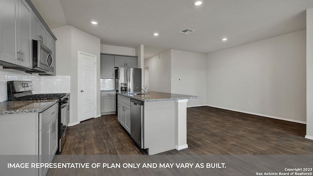 kitchen with stainless steel appliances, light stone countertops, gray cabinetry, and a center island with sink