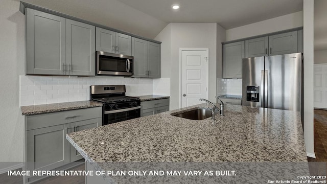 kitchen with sink, backsplash, a kitchen island with sink, light stone counters, and stainless steel appliances