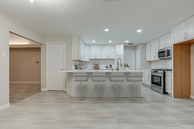 kitchen featuring sink, appliances with stainless steel finishes, white cabinetry, a kitchen bar, and kitchen peninsula