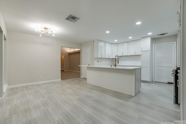 kitchen featuring stainless steel electric stove, sink, white cabinets, a center island with sink, and light hardwood / wood-style flooring