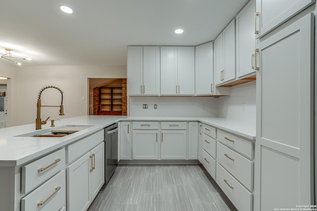 kitchen featuring white cabinetry, sink, stainless steel dishwasher, kitchen peninsula, and light stone countertops