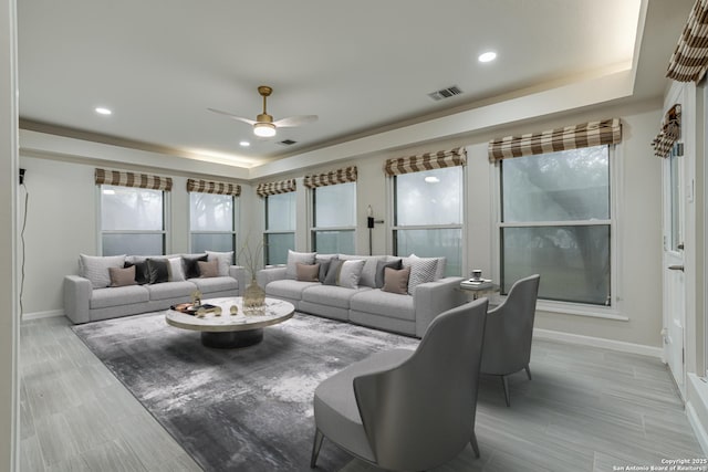 living room with ceiling fan, a raised ceiling, and light wood-type flooring