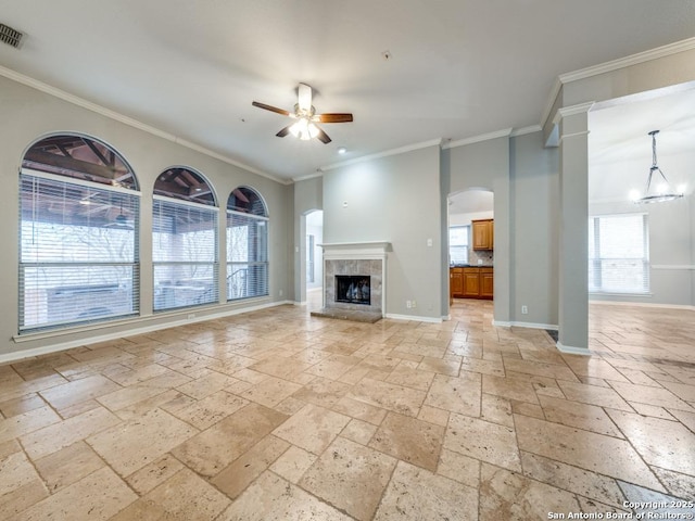 unfurnished living room featuring crown molding, ceiling fan, a tiled fireplace, and ornate columns