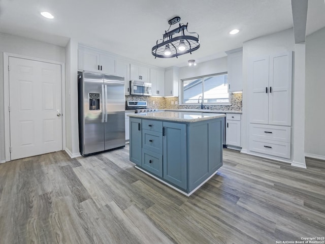 kitchen featuring appliances with stainless steel finishes, decorative light fixtures, tasteful backsplash, white cabinetry, and a center island