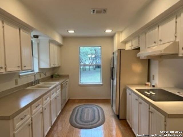 kitchen featuring sink, light wood-type flooring, white dishwasher, black electric stovetop, and white cabinets