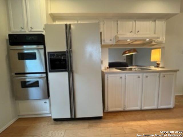 kitchen with white cabinetry, stainless steel double oven, black electric stovetop, and white refrigerator with ice dispenser