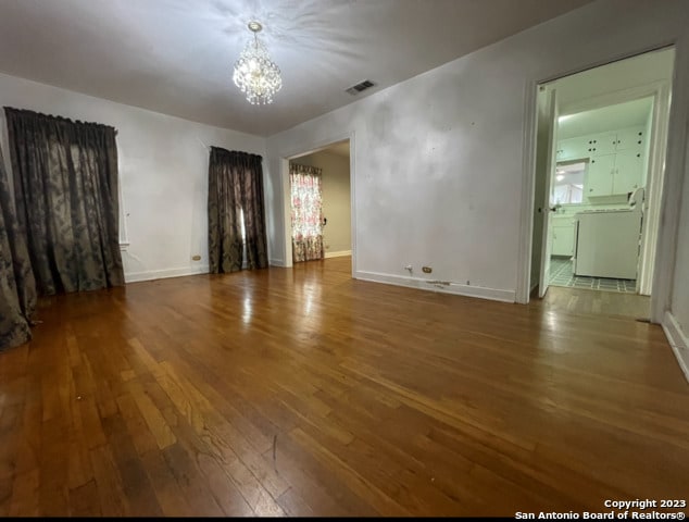 spare room featuring washer / clothes dryer, a notable chandelier, and dark hardwood / wood-style floors