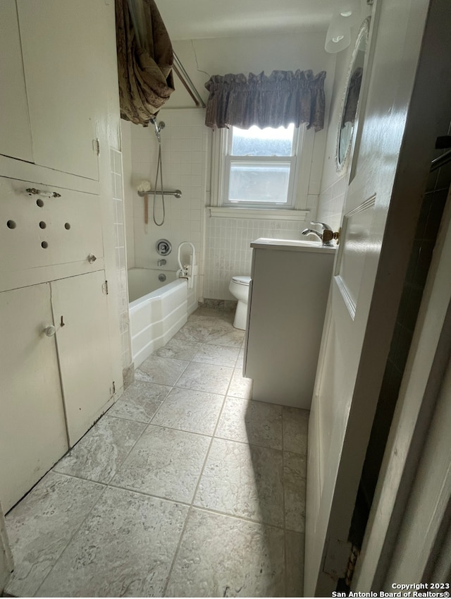 full bathroom featuring vanity, toilet, tiled shower / bath combo, and tile walls