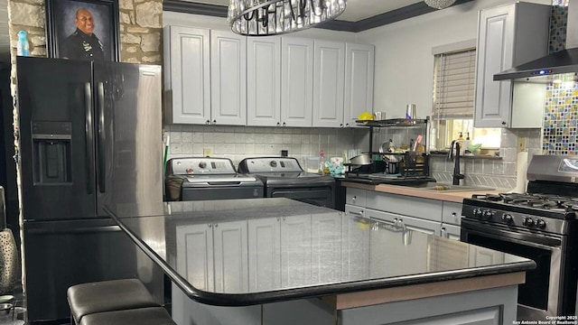 kitchen with washing machine and clothes dryer, wall chimney exhaust hood, black fridge with ice dispenser, sink, and stainless steel range with gas stovetop