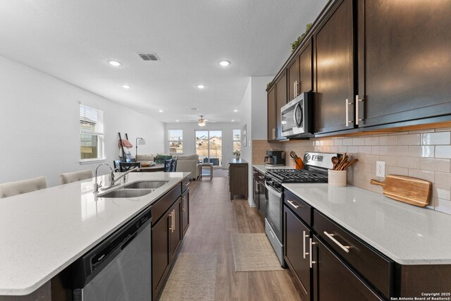 kitchen featuring stainless steel appliances, light stone countertops, sink, and a center island with sink