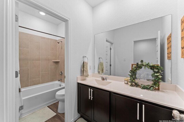 full bathroom with tiled shower / bath, hardwood / wood-style floors, vanity, and toilet