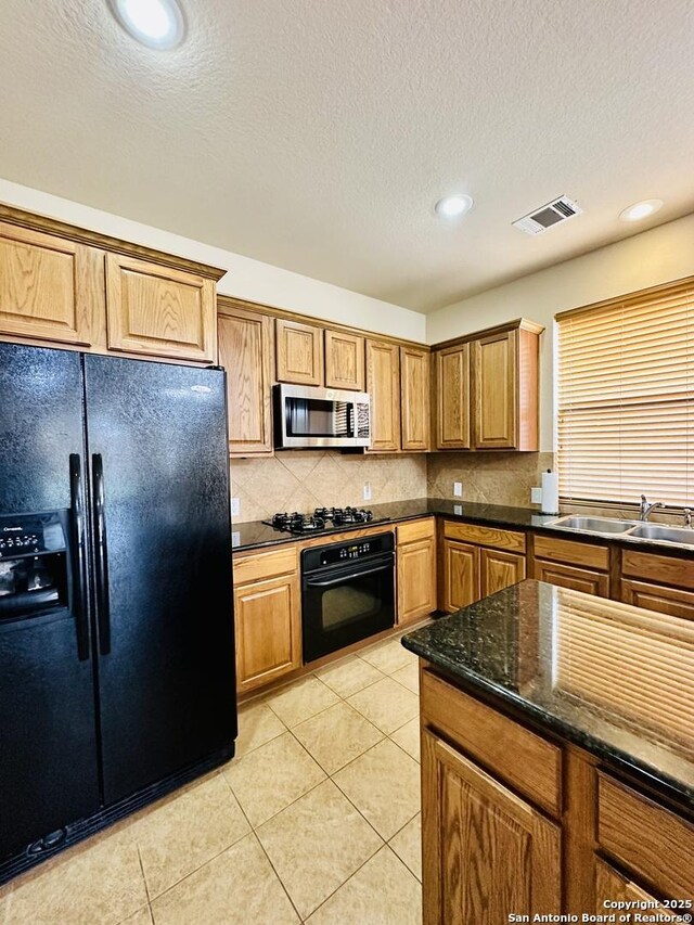 kitchen with light tile patterned flooring, sink, tasteful backsplash, dark stone countertops, and black appliances