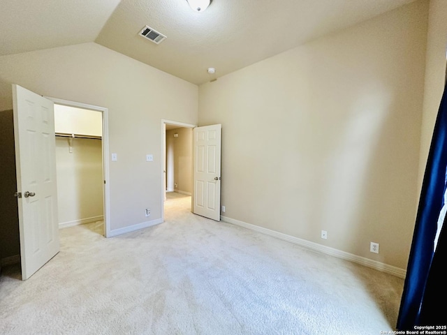 unfurnished bedroom featuring lofted ceiling, a walk in closet, light colored carpet, and a closet