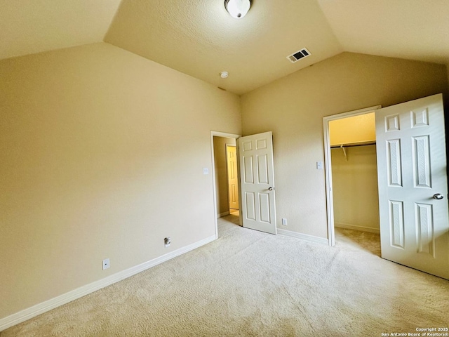 unfurnished bedroom with light carpet, a spacious closet, vaulted ceiling, and a closet