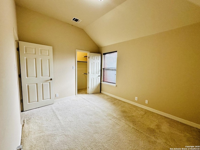 unfurnished bedroom with a spacious closet, vaulted ceiling, and carpet