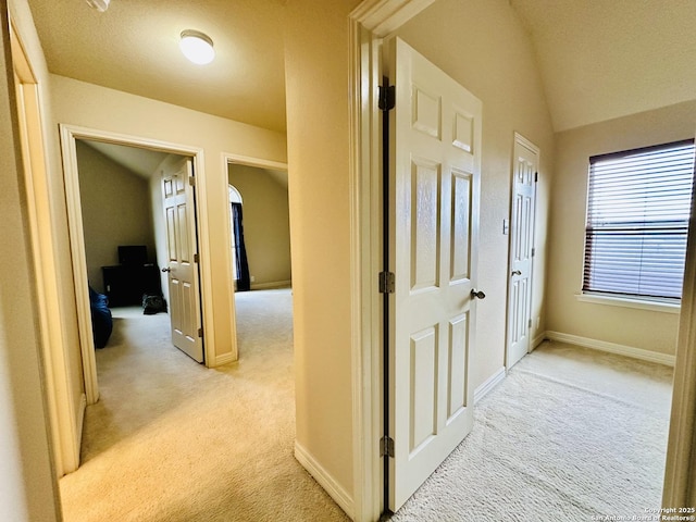 hallway featuring lofted ceiling and light colored carpet