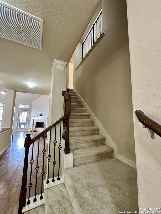 stairs featuring hardwood / wood-style flooring, a tile fireplace, and a textured ceiling