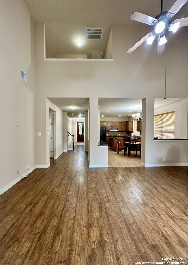 unfurnished living room featuring a towering ceiling, ceiling fan with notable chandelier, and light wood-type flooring