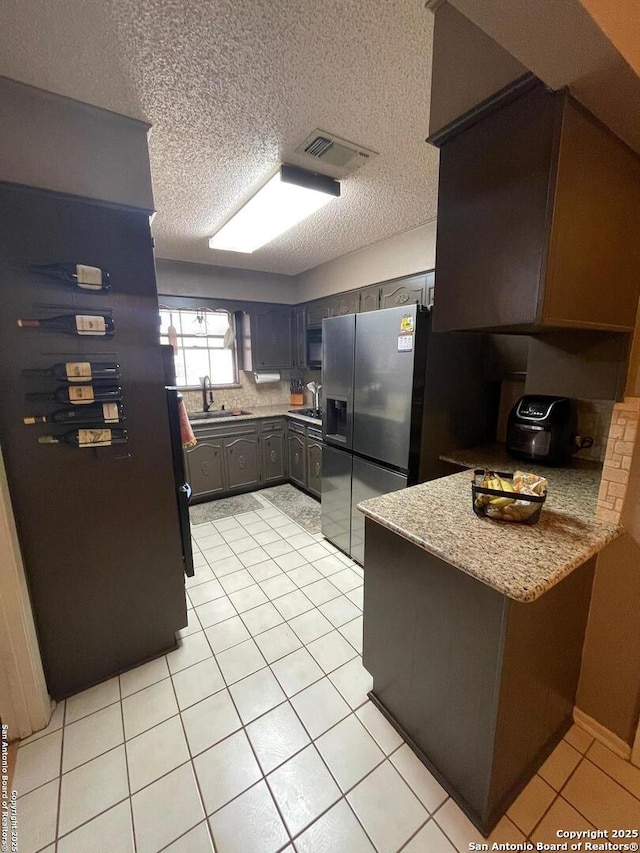 kitchen featuring sink, stainless steel fridge with ice dispenser, dark brown cabinets, light tile patterned floors, and light stone countertops