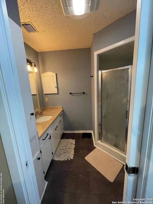 bathroom with tile patterned flooring, vanity, an enclosed shower, and a textured ceiling