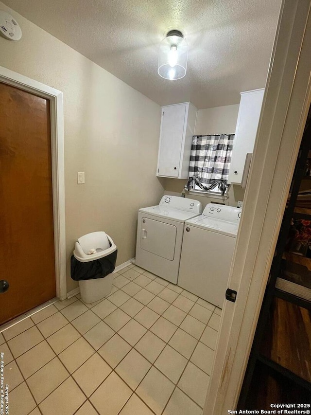 laundry area with a textured ceiling, cabinets, washing machine and clothes dryer, and light tile patterned flooring