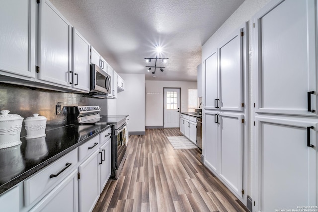 kitchen with tasteful backsplash, white cabinetry, wood-type flooring, stainless steel appliances, and a textured ceiling