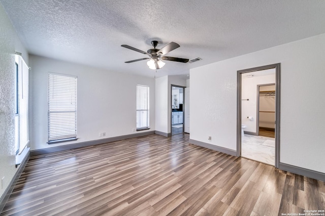 unfurnished bedroom featuring wood-type flooring, ensuite bathroom, ceiling fan, and a textured ceiling