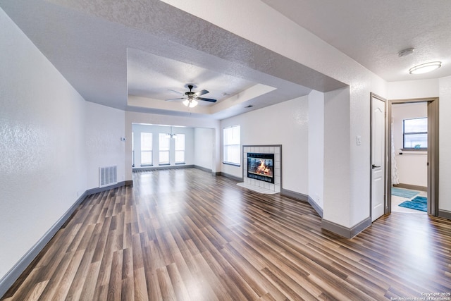 unfurnished living room with a raised ceiling, a tiled fireplace, dark hardwood / wood-style floors, and a textured ceiling