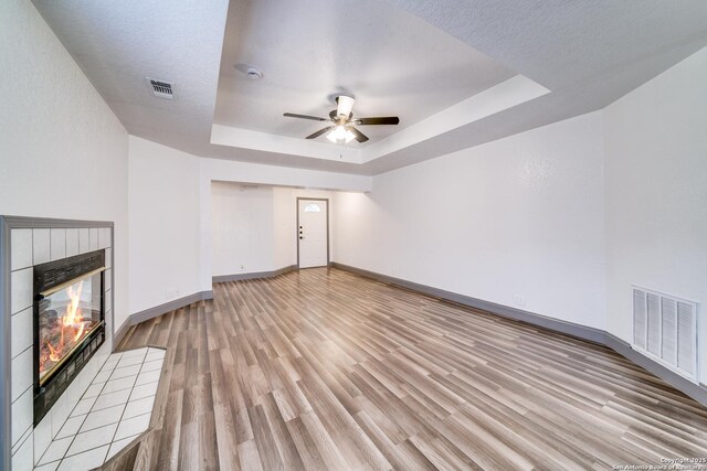 unfurnished living room featuring a fireplace, a raised ceiling, light hardwood / wood-style flooring, and a textured ceiling