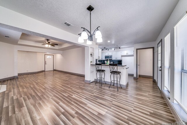 interior space featuring a breakfast bar area, a textured ceiling, white cabinets, decorative light fixtures, and light wood-type flooring